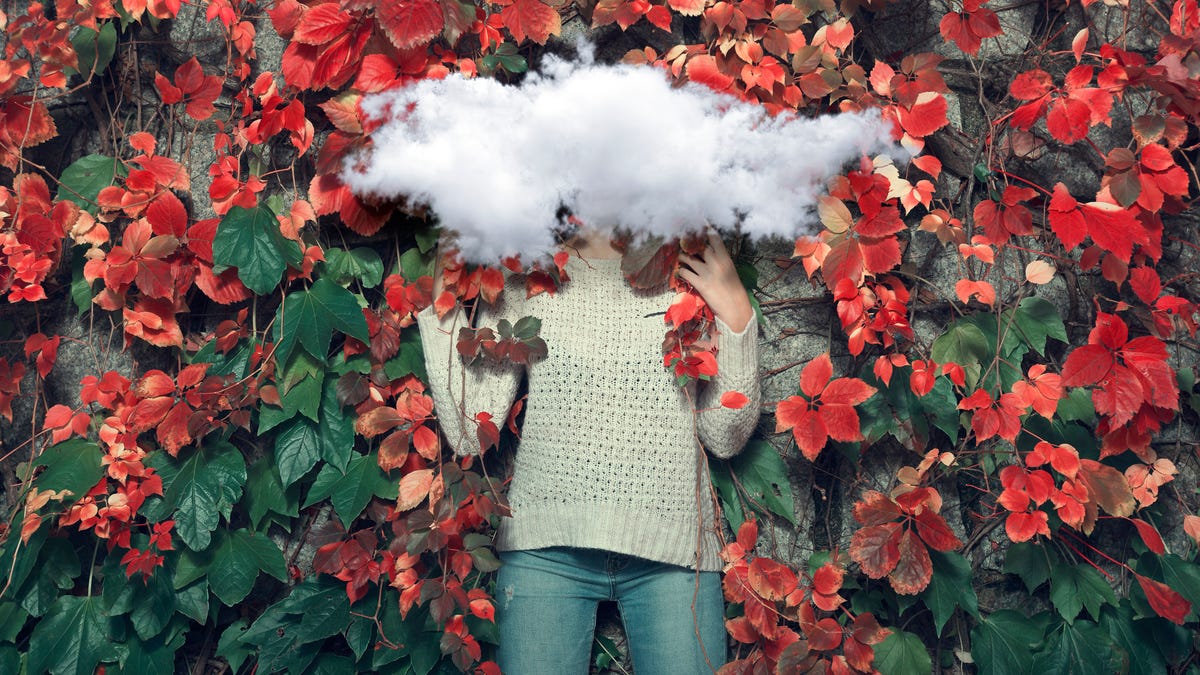 Concept of clouded thinking. Portrait of a women standing in from of a wall with a cloud on her head.