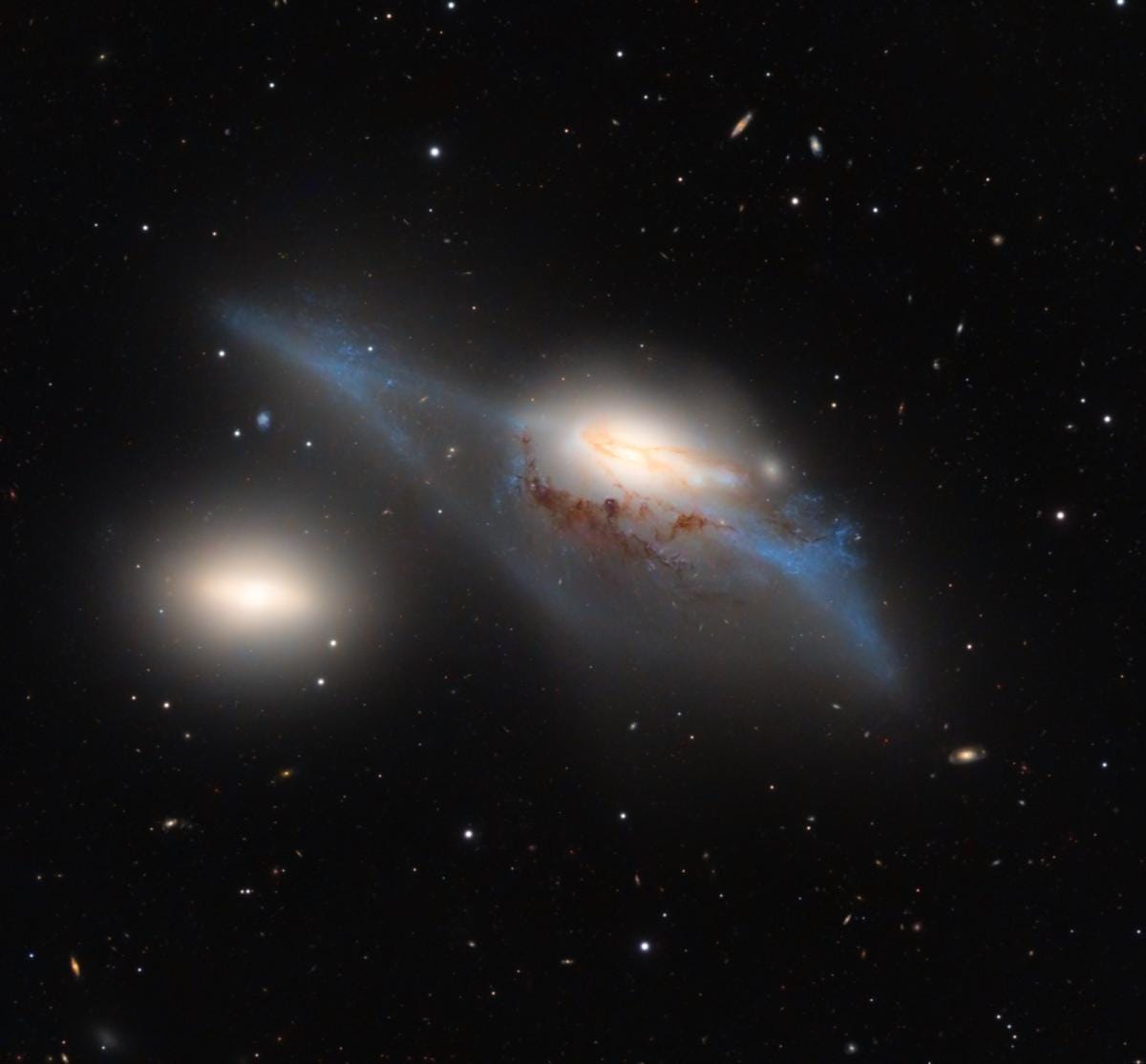 Interacting galaxy looks like two glowing blobs of fuzzy material against a star and galaxy-studded backdrop.