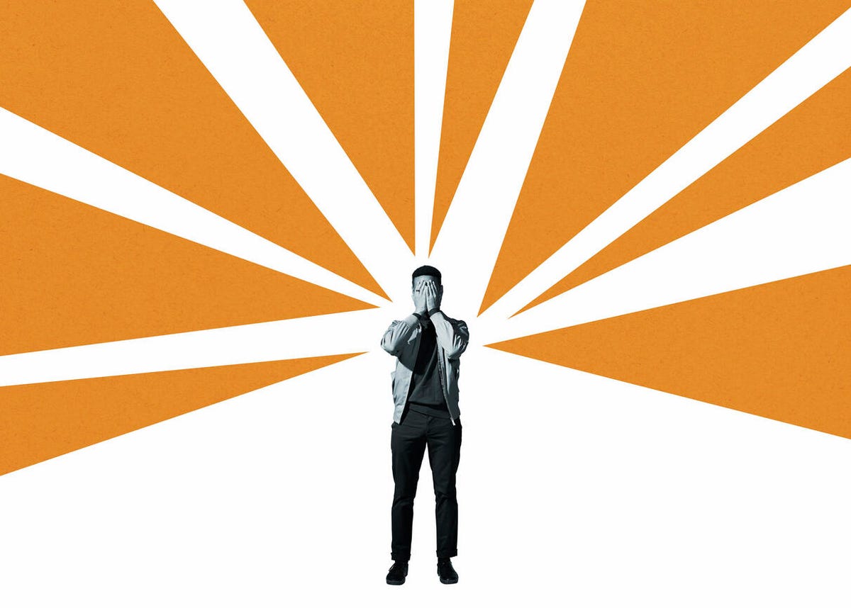 Anxious man covering face with hands while standing amidst orange rays against white background