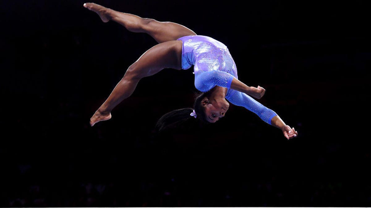 Simone Biles does a flip on a balance beam.