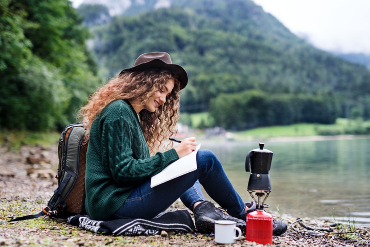 Hiker taking a break by a lake while writing in her journal.