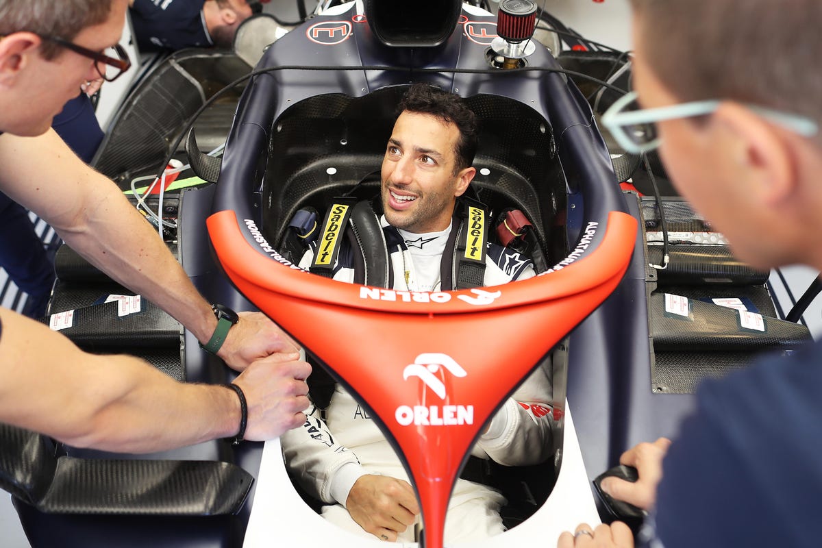 Daniel Ricciardo is smiling as he sits in the AlphaTauri race car.