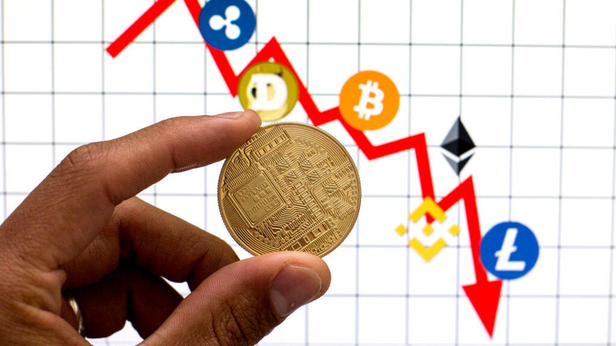 An image of someone holding a crypto coin against a backdrop of a chart showing a plunge in crypto prices.