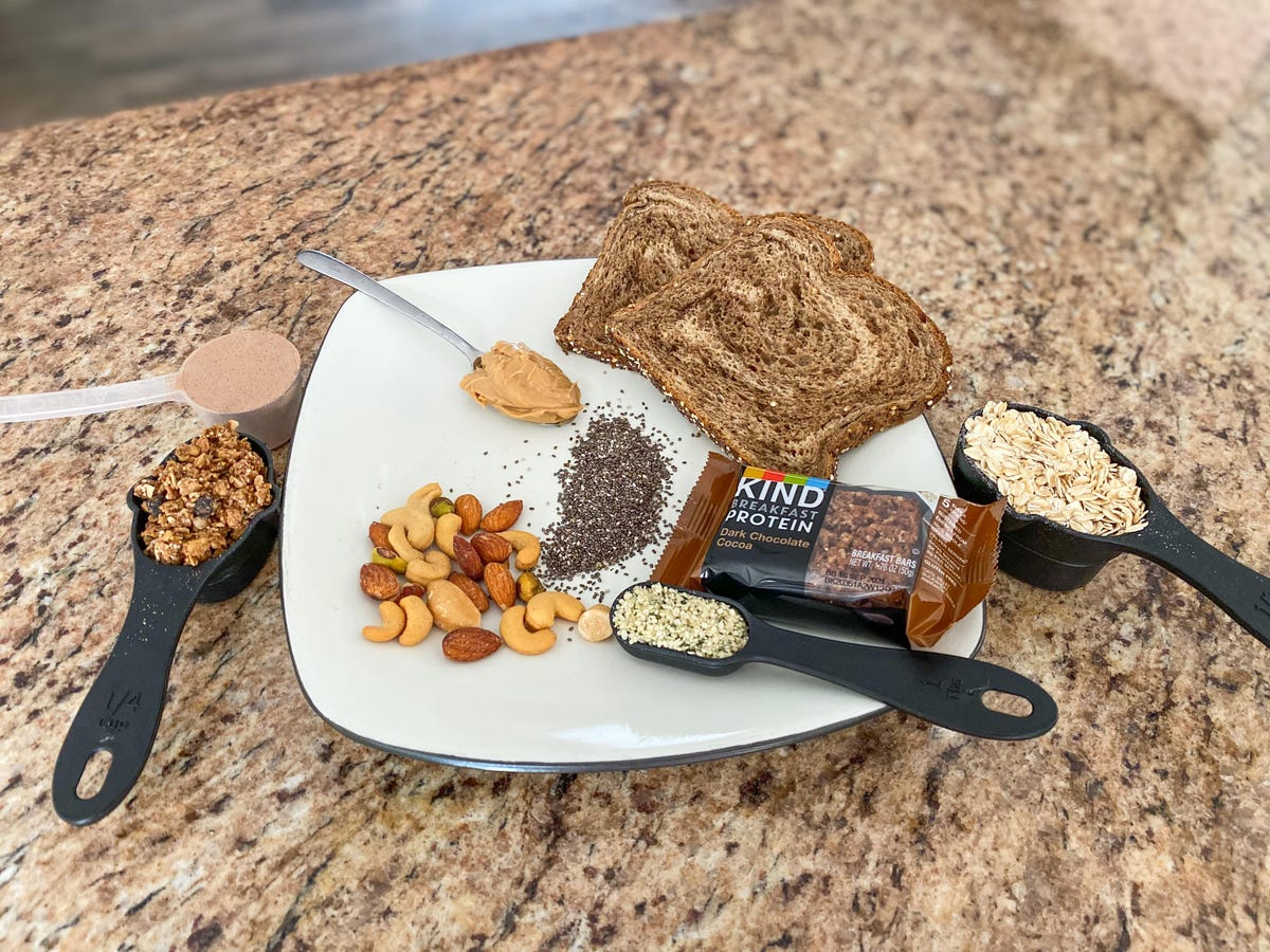 a spread of food containing granola, protein powder, hemp seeds, peanut butter, chia seeds, bread, oats, and a granola bar depicting protein options for vegans