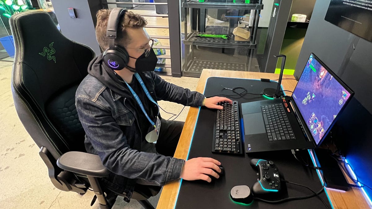 A man sits at a computer playing a game, feeling haptic feedback through headphones using Razer's new software developer kit.