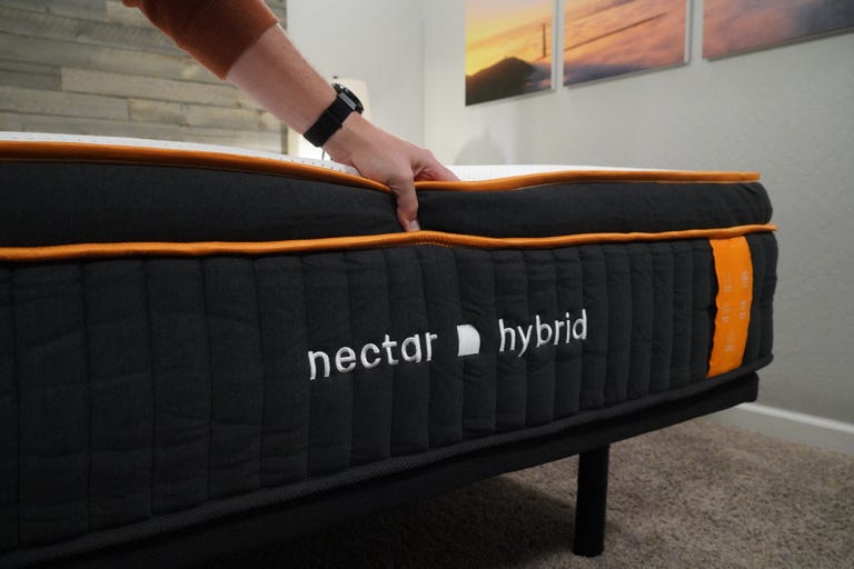 The Nectar Premier Copper Hybrid mattress sits on a bed frame while a hand pushes down on the top of the mattress.
