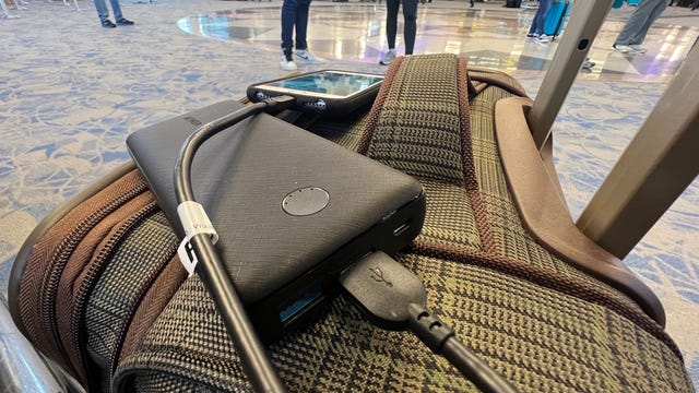 In a busy airport, a power bank rests on a suitcase, plugged into a phone.