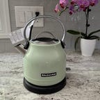 A pistachio green-colored KitchenAid KEK1222 electric kettle sits on a granite countertop.
