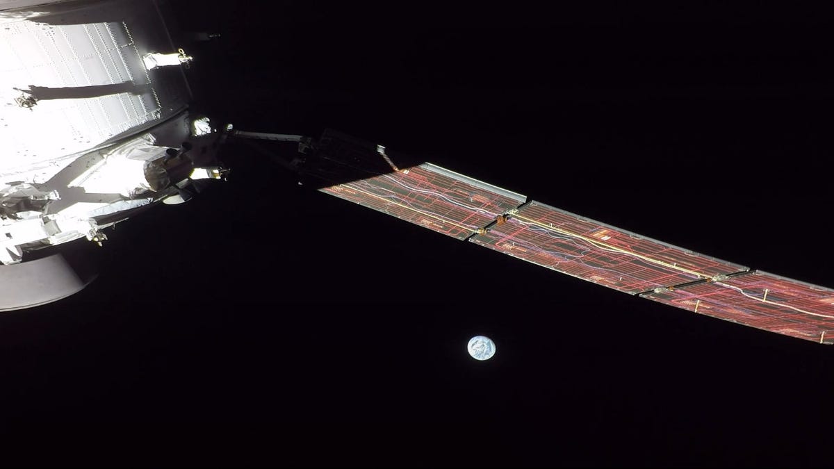 Part of the white Orion spacecraft and an extended solar array against black space with the partially lit Earth looking dainty.