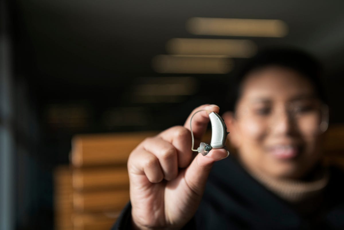Person holding over-the-ear hearing aid.
