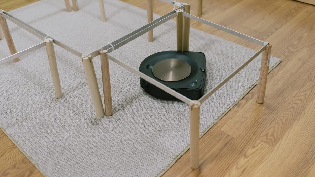 A robot vacuum cleans around table legs.