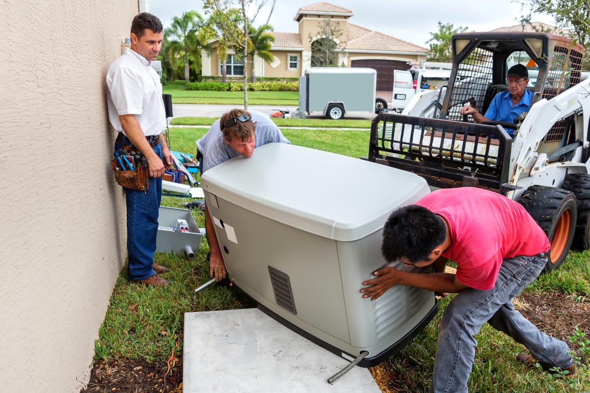 Four individuals move a generator into place with the help of a small loader.