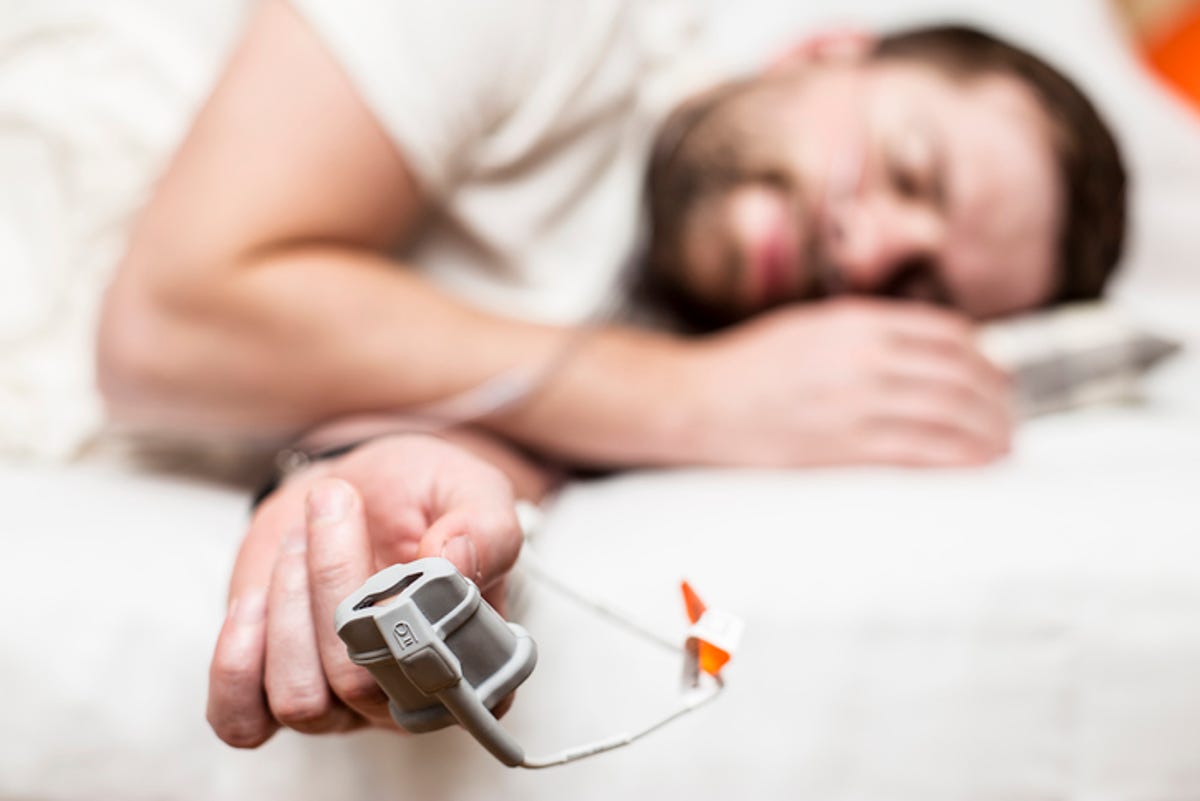 Man sleeping with a sleep apnea diagnostic device on finger.