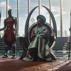 Queen Ramonda, played by Angela Bassett, sits on the Wakanda throne surrounded by warriors and members of court.