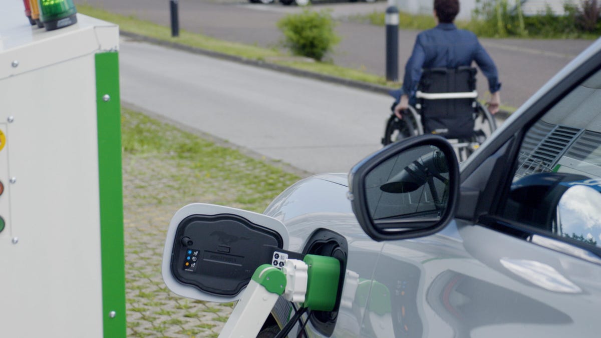 A car plugged into Ford&apos;s new robot charger with a wheelchair user in the background