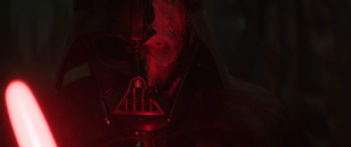 Darthas Vaderis, jo šalmas sulaužytas ir atidengęs apdegusį Anakino Skywalkerio veidą, pakelia raudoną šviesos kardą prie Obi-Wan Kenobi.