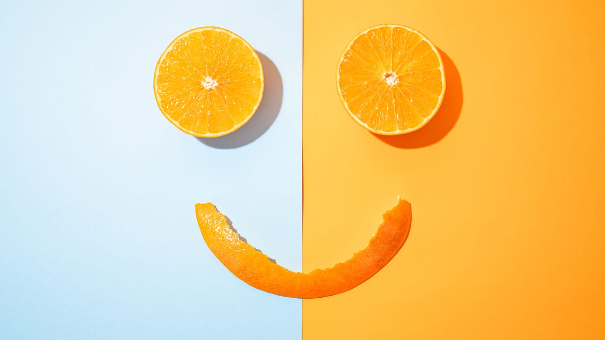 Halved and peeled oranges making a smiley face on blue and orange-colored background.