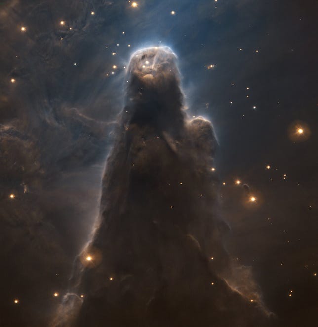 A spooky gray cloud-like nebula in the shape of a ghostly almost human-like form as stars glimmer in and around it.