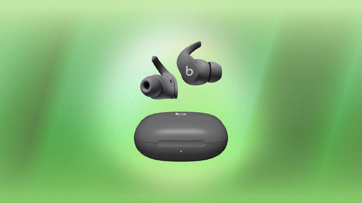 A pair of gray Beats Fit Pro earbuds and charging case against a green background.