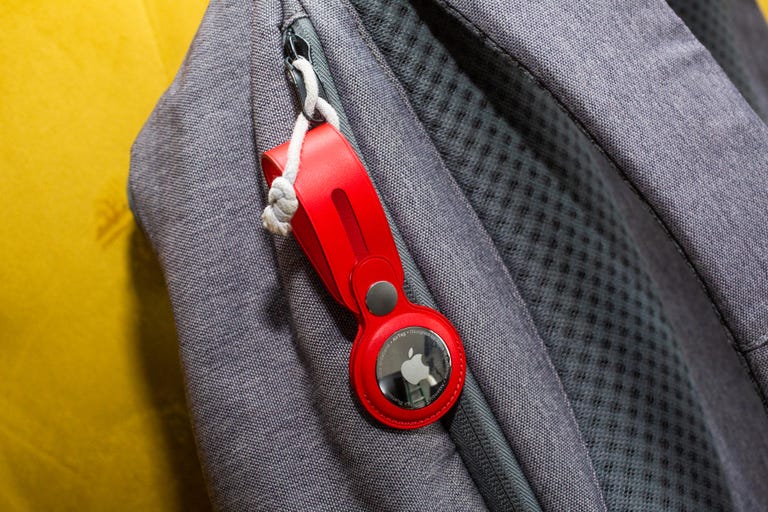 A red AirTag hanging from a zipper-pull on a gray backpack.