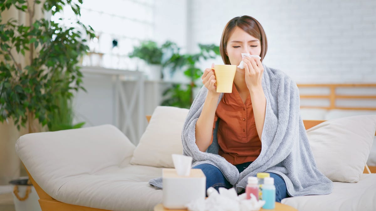 Woman battling a cold, drinking tea and blowing her nose