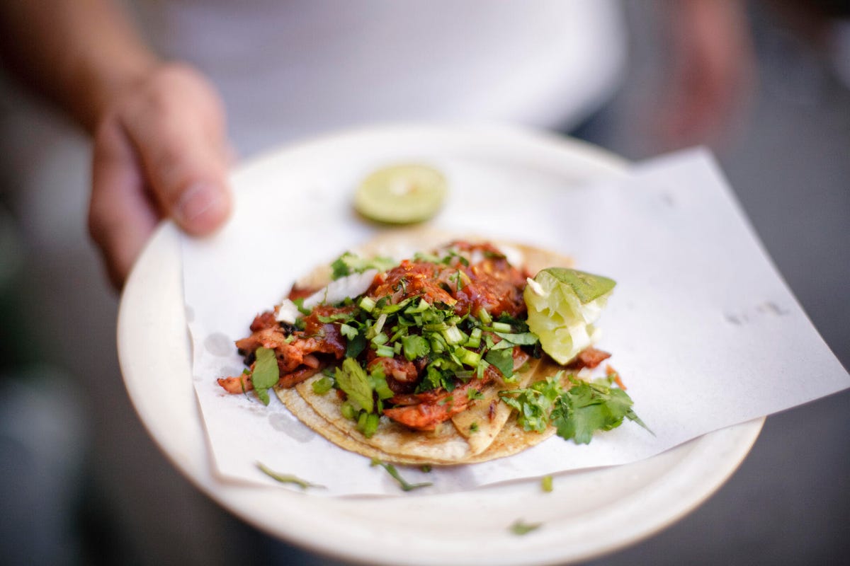 Close-up of a street taco on a plate, served with garnishes and lime.