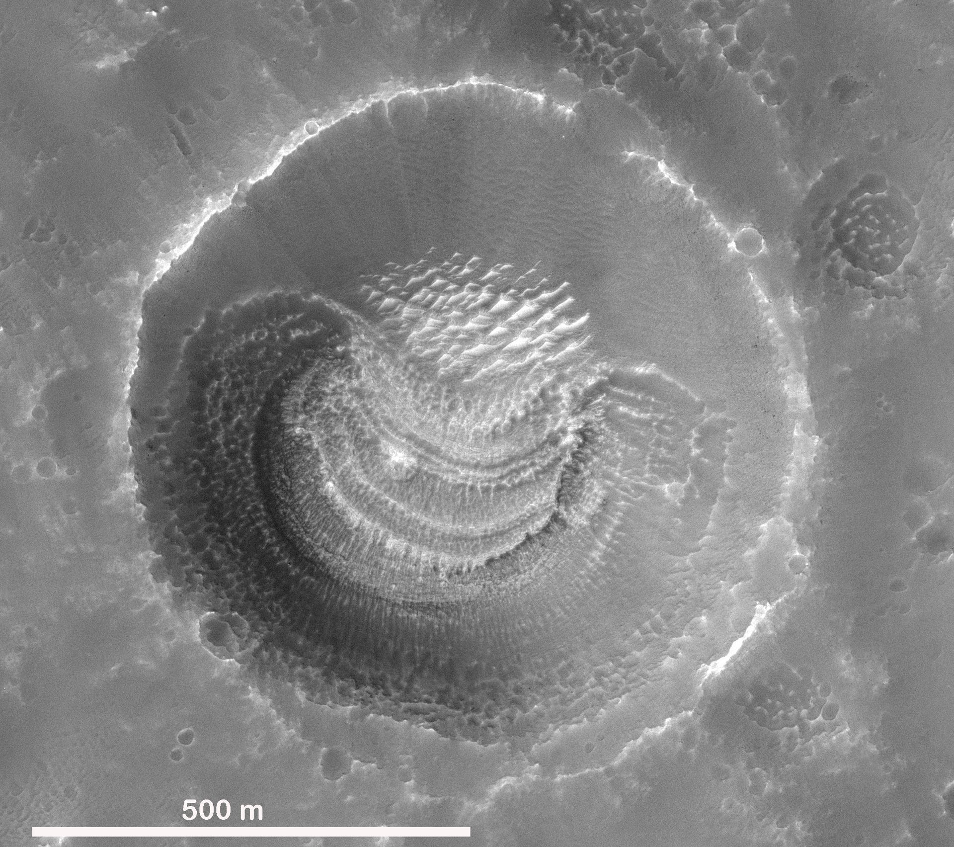 Black-and-white, overhead view of a Mars impact crater with unusual layered deposits on the south side.