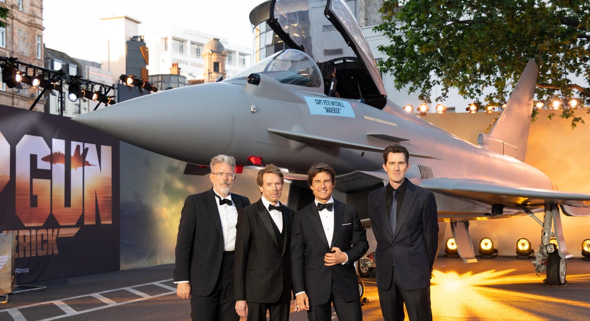 Filmmakers Christopher McQuarrie, Jerry Bruckheimer, Tom Cruise and Joseph Kosinski in black tie standing in front of a fighter plane at the UK premiere of Top Gun: Maverick.