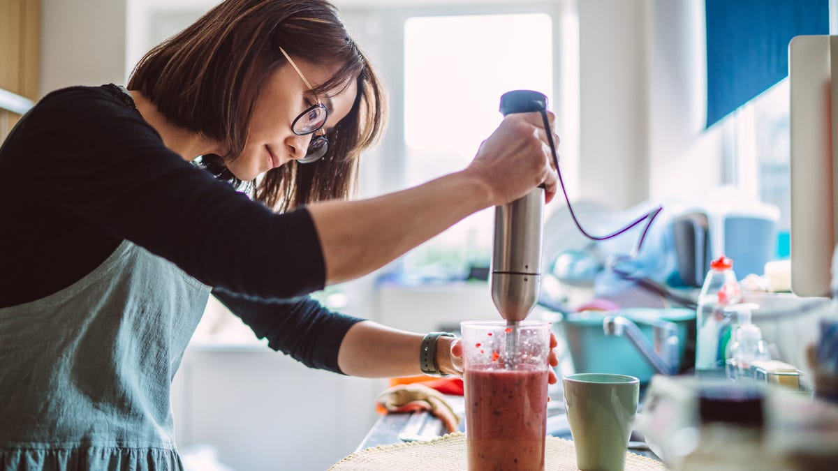 Woman makes a fruit smoothie with an immersion blender.