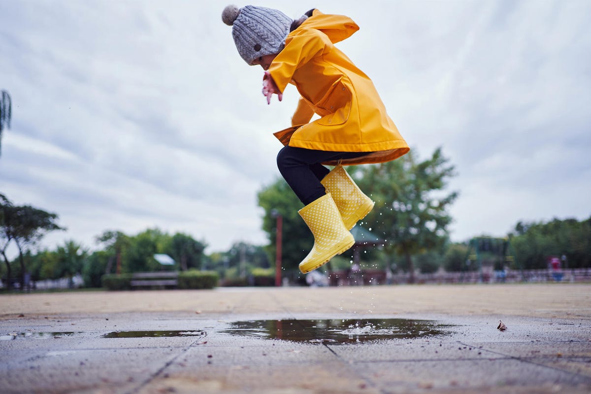 Un niño pequeño pisando fuerte en un charco con botas de lluvia