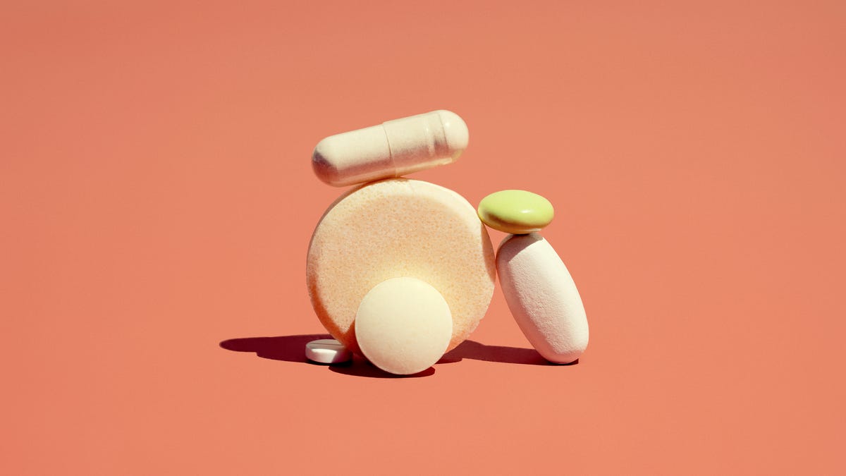 Bunch of different vitamins on a flat surface against a coral-colored background