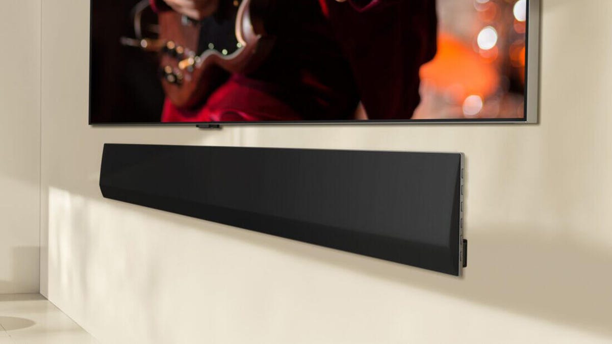 LG&apos;s 2024 sound bar sitting on a white ledge under a TV on a white wall.