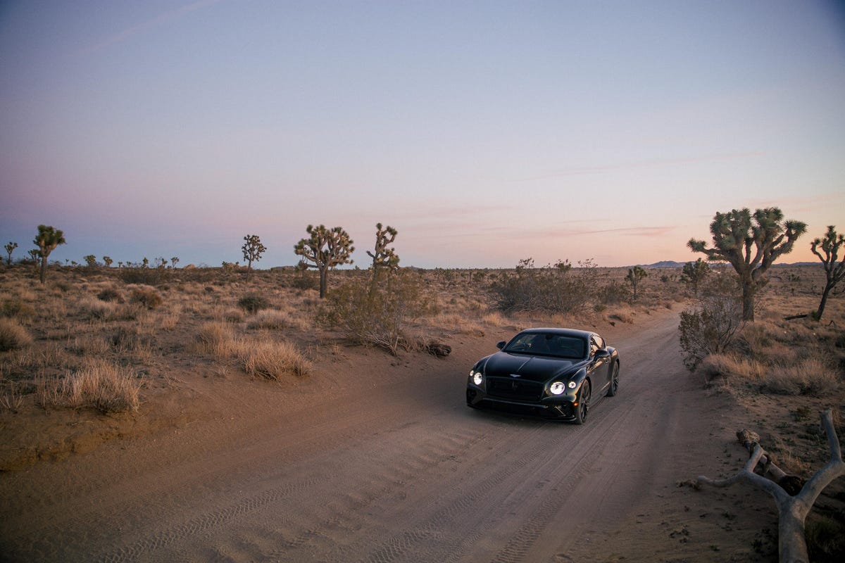 Far-away front 3/4 view of a green 2022 Bentley Continental GT Speed Coupe in the desert