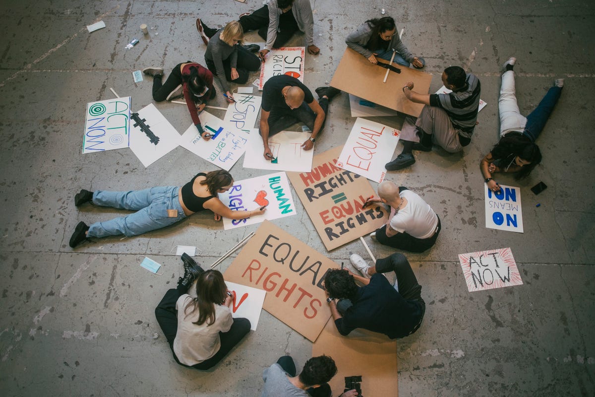 Yerde oturan gençler, insan hakları ve eşit haklar hakkında protesto afişleri yapıyor