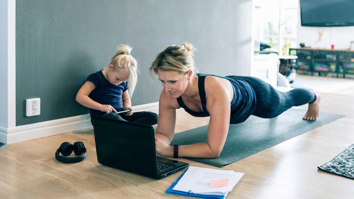 woman working on a laptop while in plank position on yoga mat, with a child next to her