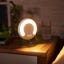 The Amazon Halo Rise with its light turned on pictured on a nightstand in a dim bedroom.