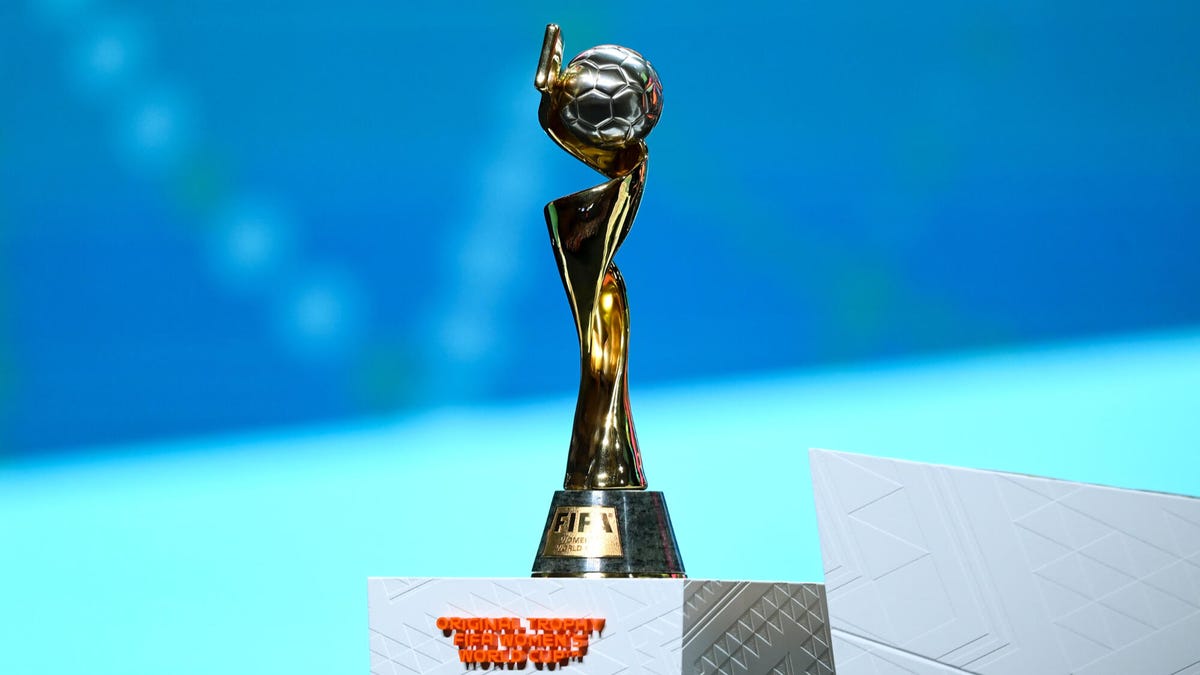 El trofeo ganador de la Copa Mundial Femenina de la FIFA se encuentra sobre un pedestal frente a un fondo azul.