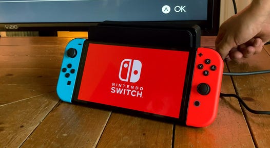 a Nintendo Switch OLED with red and blue controllers sits next to a TV
