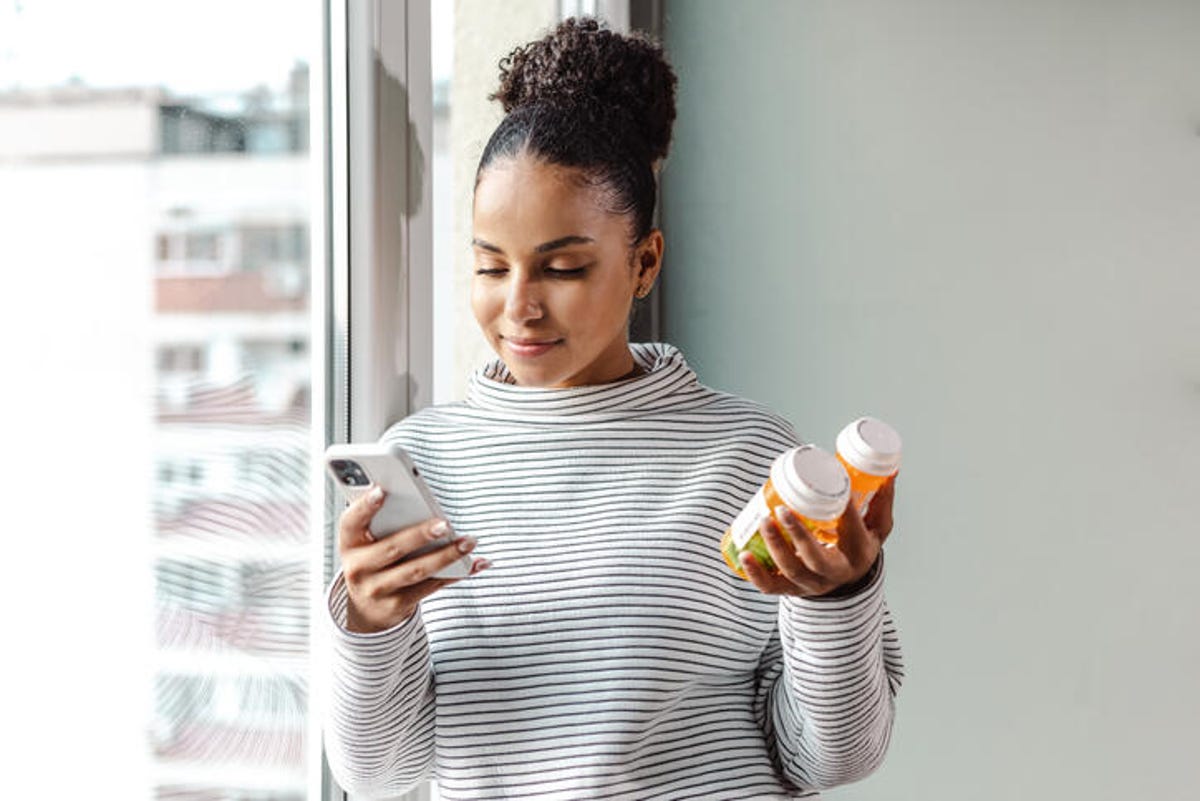 Woman using her phone while holding pill bottles.