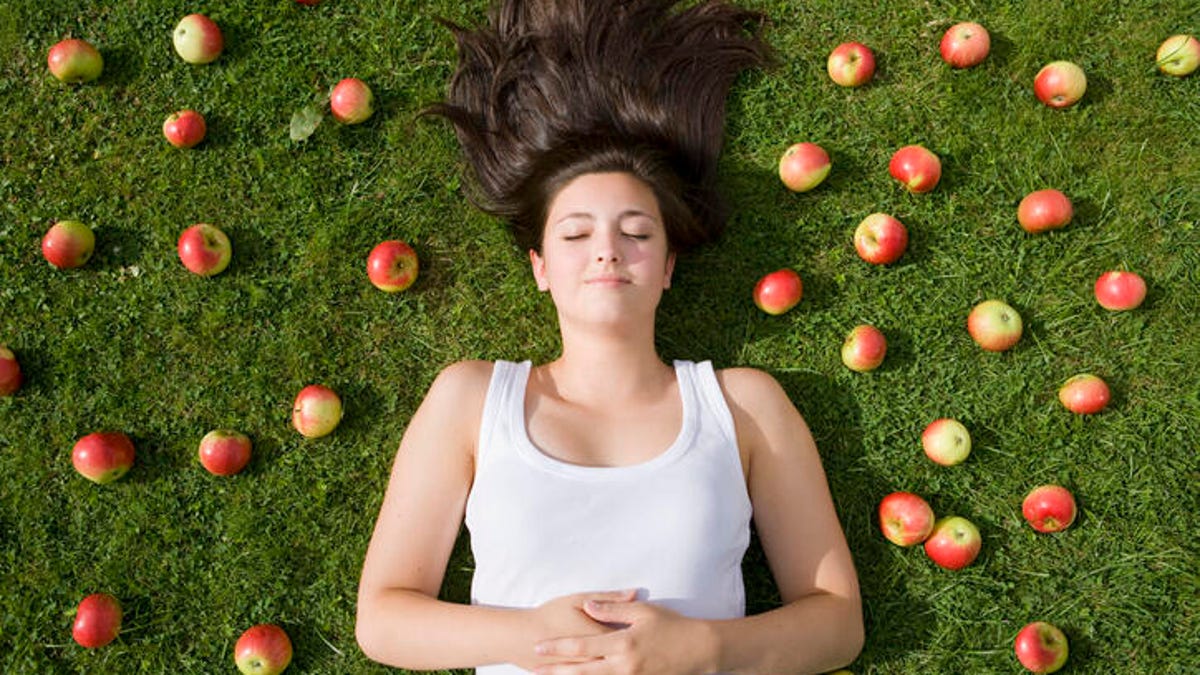 Woman lying on the grass with apples all around her.