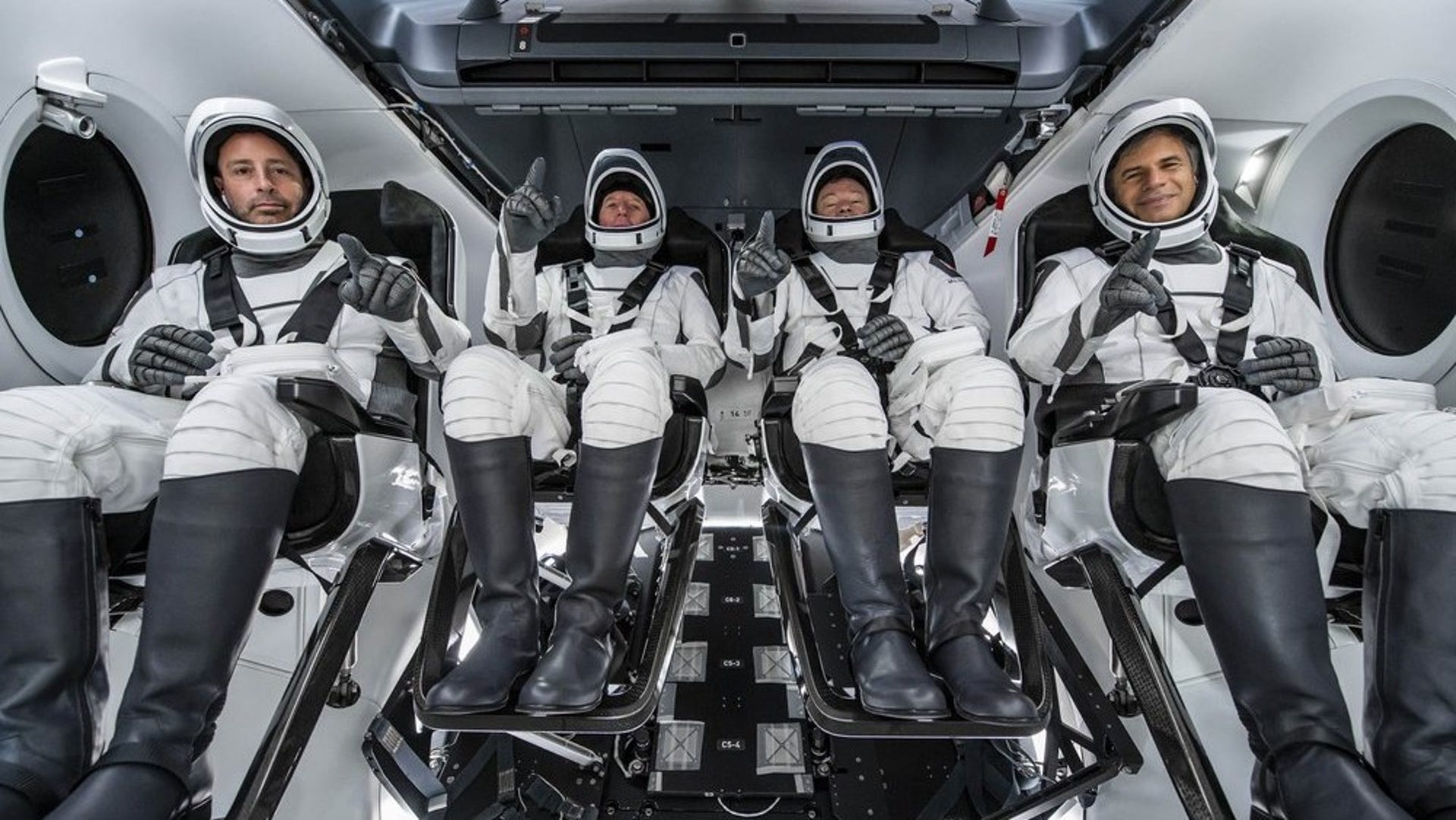 Four private astronauts pose in suits inside a SpaceX capsule.