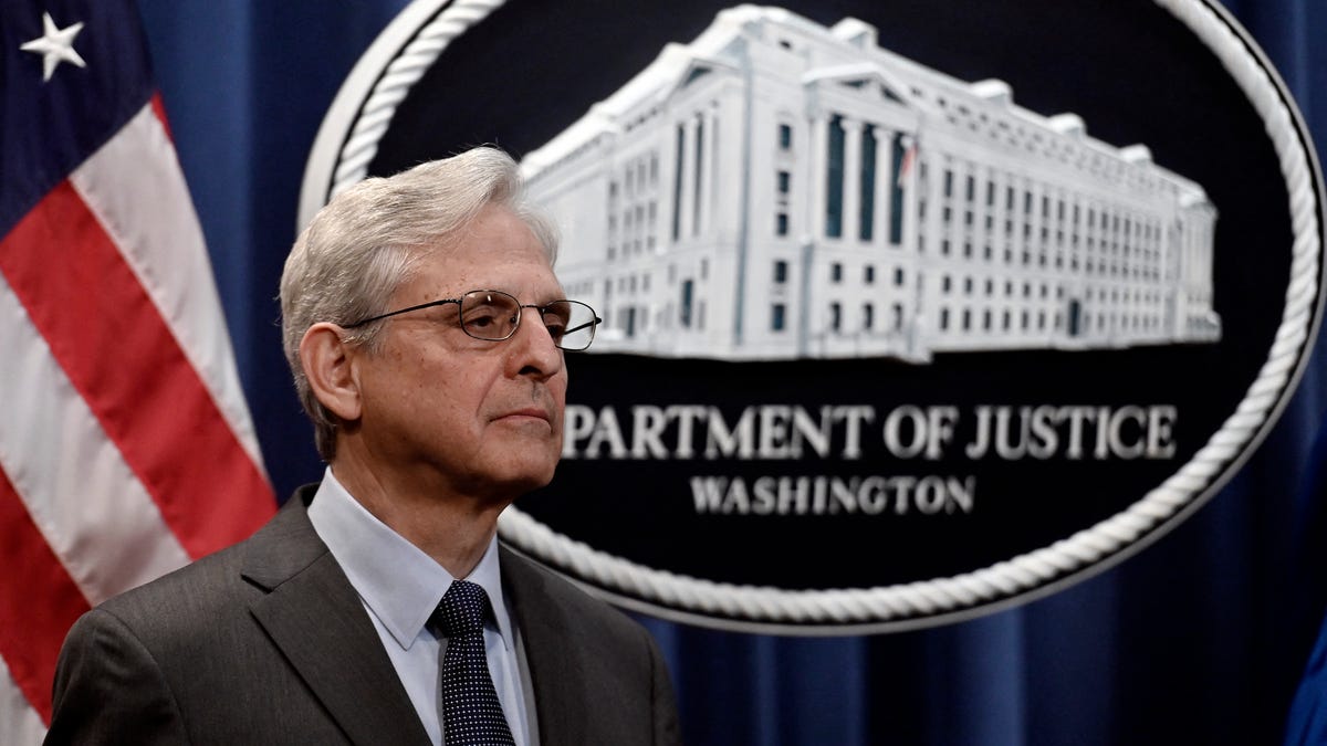 Merrick Garland stands in front of Department of Justice emblem.