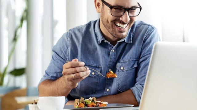 A man eats a meal from ModifyHealth while chatting on a computer.