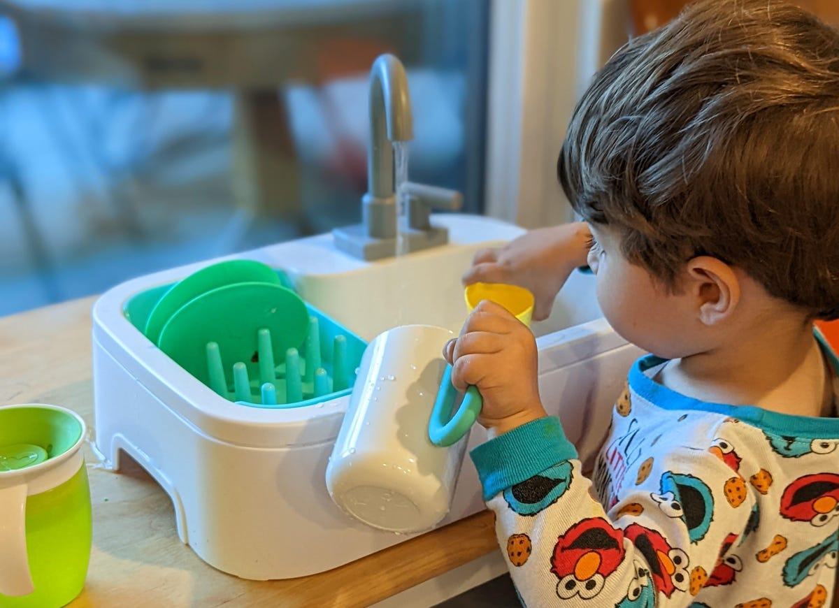 A toddler playing at a toy sink.