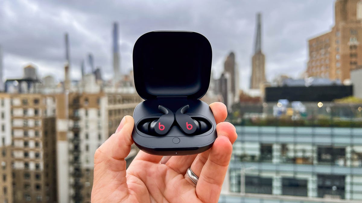 A pair of black Beats Fit Pros in their charging case being held up against a city skyline.