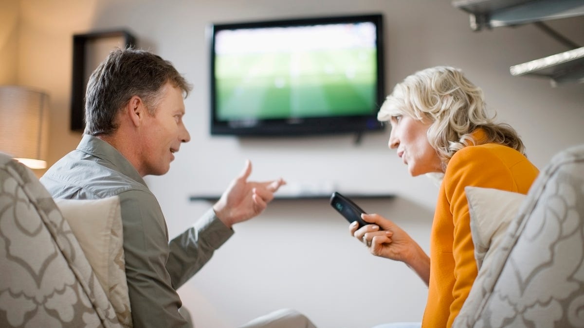 A middle-aged couple arguing over a remote control.