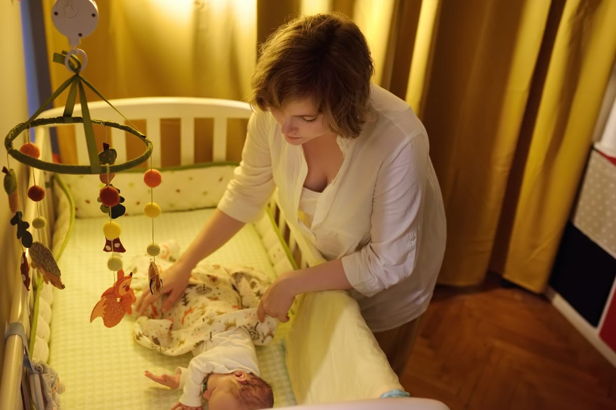 A woman puts her baby to bed in a crib lined with crib bumpers