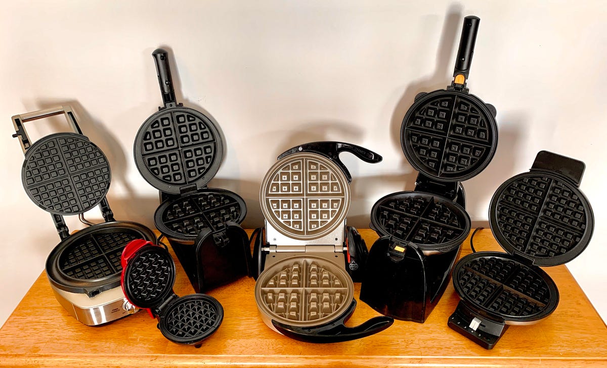 A variety of open waffle makers on a wooden table top.