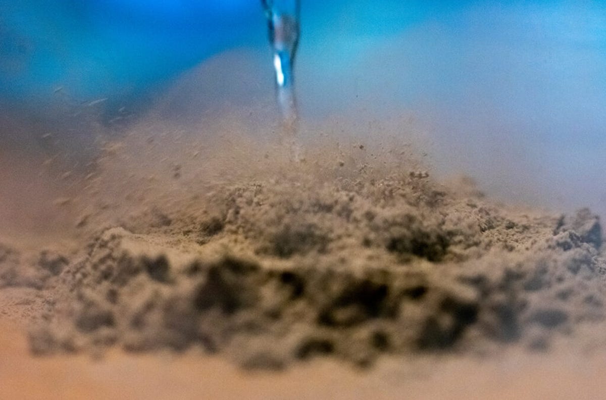 Brownish moon dust appears to be pluming upward and separating its particles as a stream of liquid comes into contact with it.