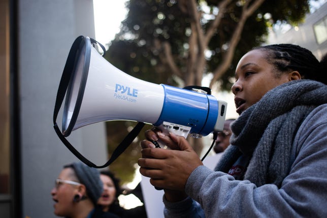 Erin Shields, the national field organizer for internet rights at MediaJustice, speaks through a megaphone during a rally outside Twitter's headquarters. 